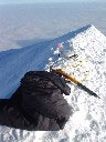 The GPS, wrapped in Damien's black jumper, on the summit. The round white antenna is next to the little red summit marker and the orange ice axe is to stop it all falling off. At this point the temp was about -30 degrees Celsius. © Geoscience Australia.