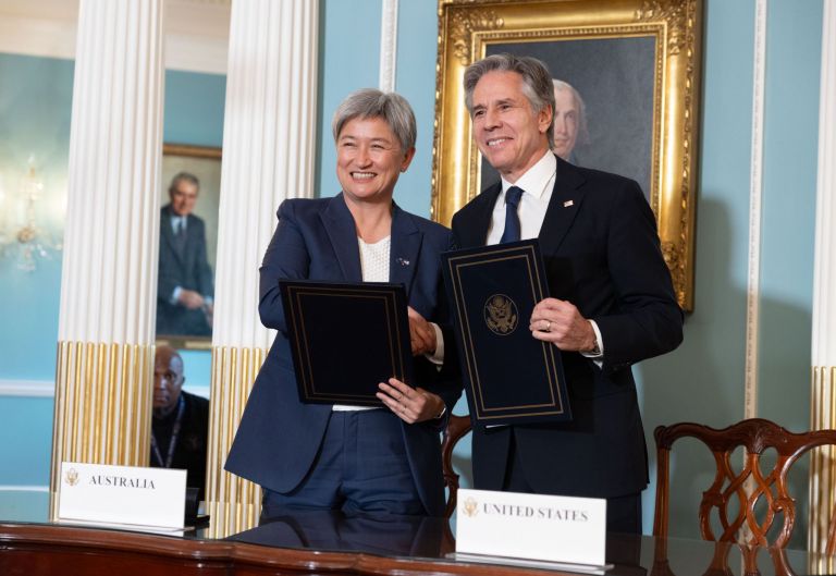 Minister Wong and Secretary of State Blinken shaking hands and holding copies of the newly-signed bilateral statement