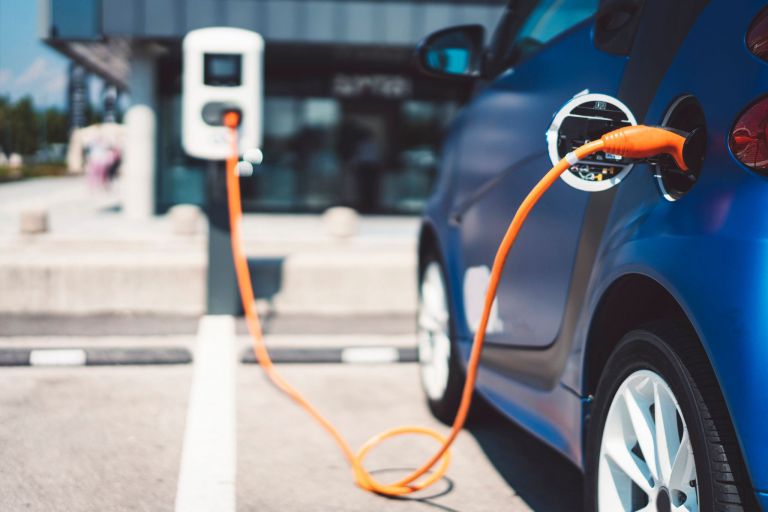 Blue electric vehicle plugged in to charge using an orange charging cable