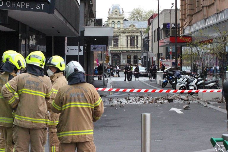 Emergency workers group in discussion on the outside of a cordoned off street that has masonry building ruble in the middle of the road that has fallen from building during the 2021 Melbourne earthquake